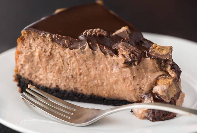 Reese Cheesecake - A chocolate and peanut butter dream! This decadent cheesecake is sandwiched by chocolate crust and chocolate ganache with a peanut butter punch.