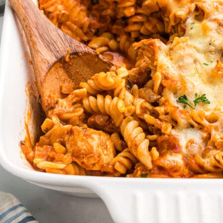 Baked chicken and tarragon pasta in a casserole dish with a wooden spoon.