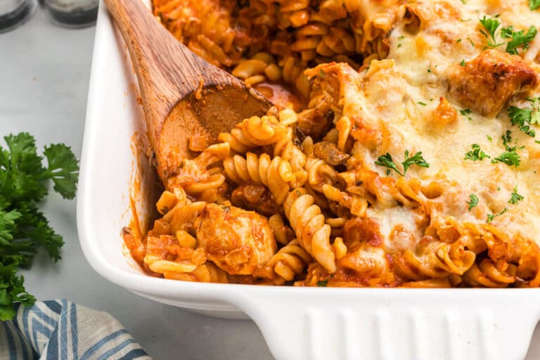 Baked chicken and tarragon pasta in a casserole dish with a wooden spoon.