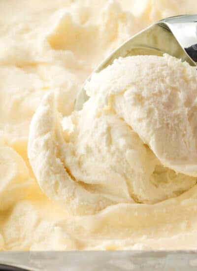 A tub of vanilla ice cream with an ice cream scoop.