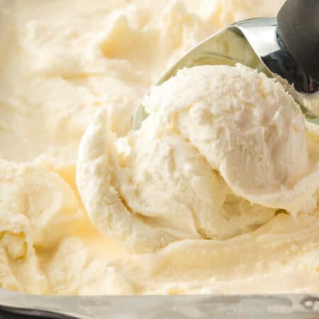 A tub of vanilla ice cream with an ice cream scoop.