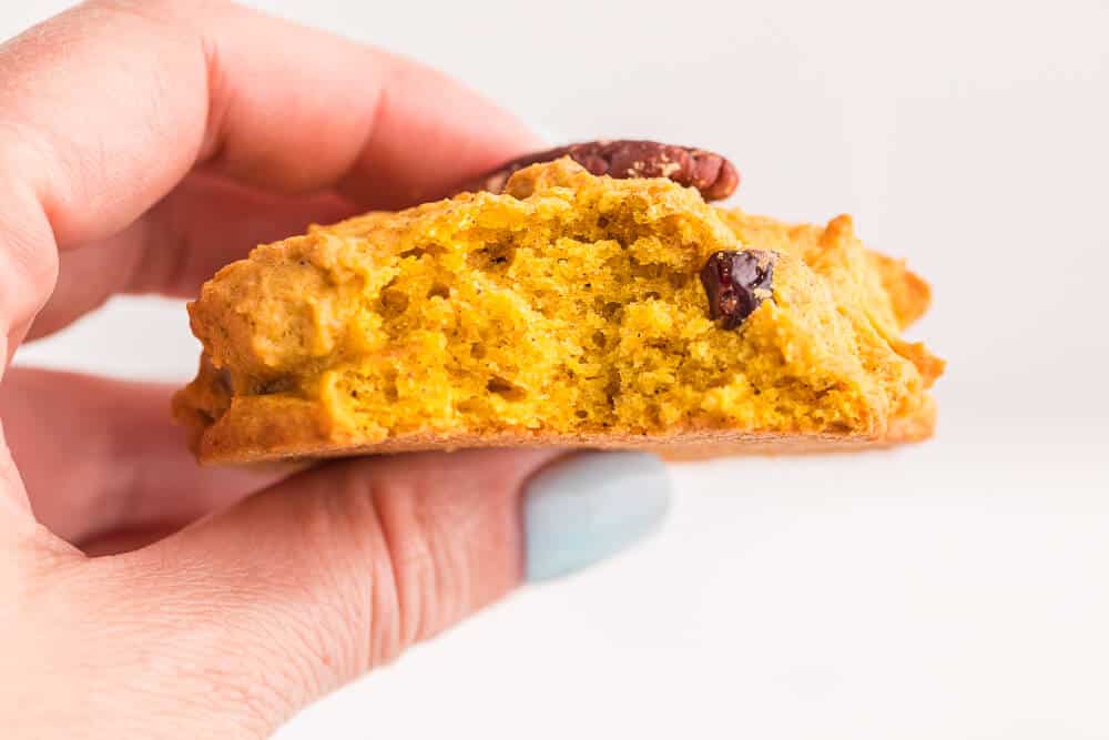 A hand holding a pumpkin breakfast cookie with a bite out of it