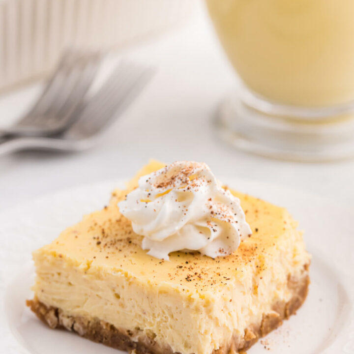 eggnog cheesecake bar topped with whipped cream on a white plate.