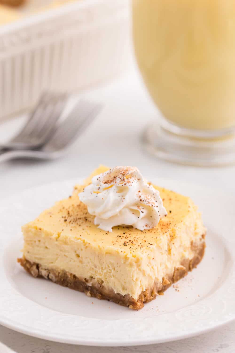 eggnog cheesecake bar topped with whipped cream on a white plate.