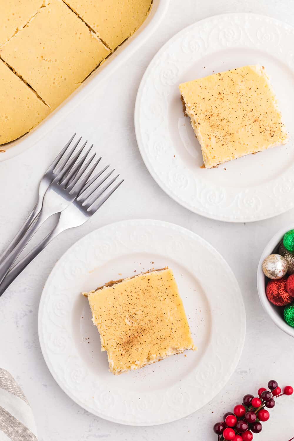 overhead of two slices of eggnog cheesecake bars on white plates.