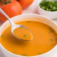 A spoon in a bowl of roasted garlic and tomato soup.