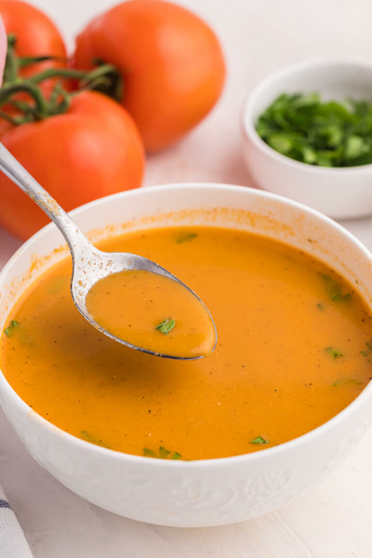 A spoon in a bowl of roasted garlic and tomato soup.
