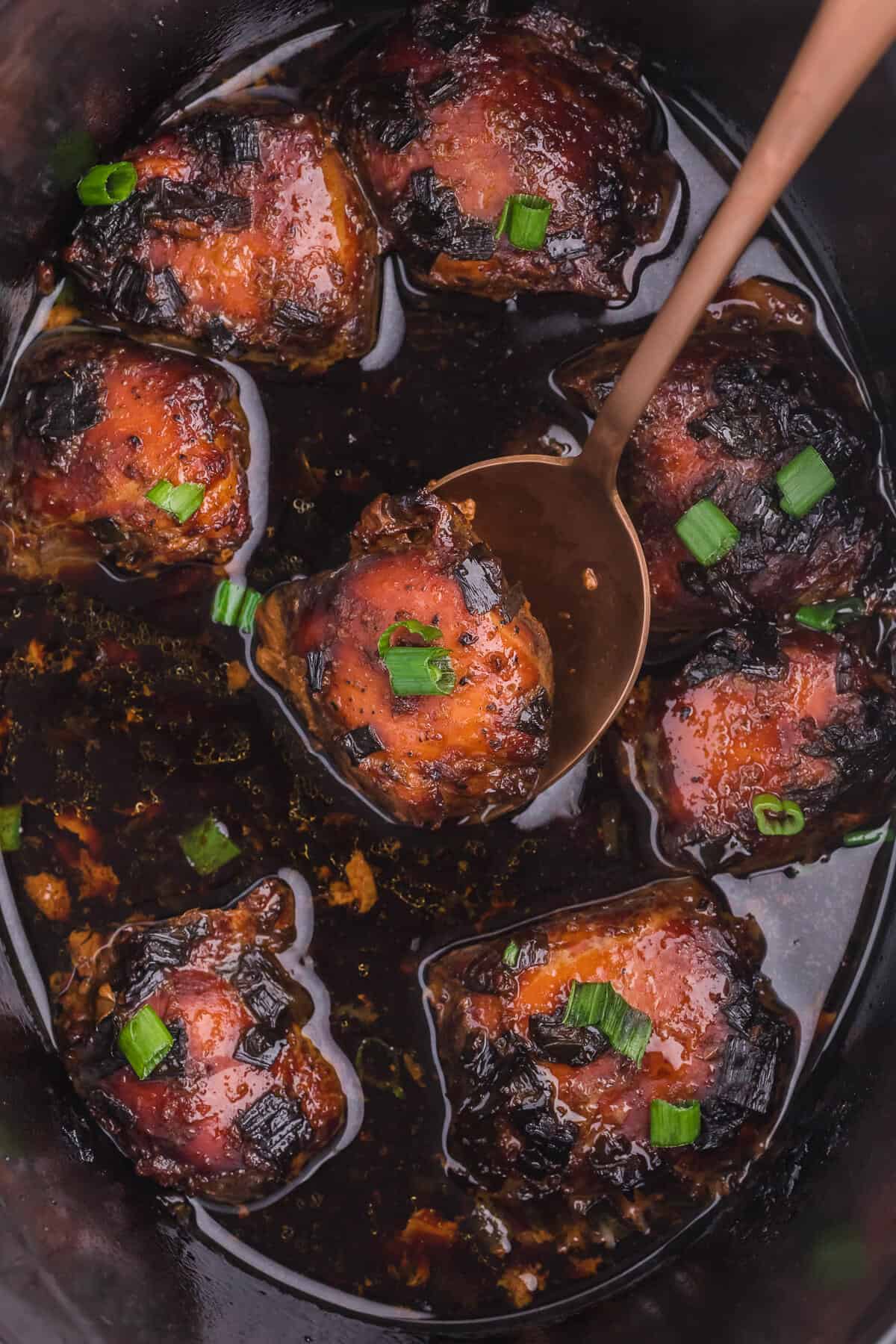 close up image of peking chicken in the slow cooker with a serving spoon