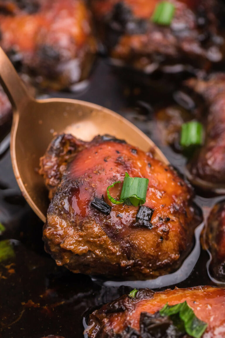 A chicken thigh on a serving spoon in a slow cooker.