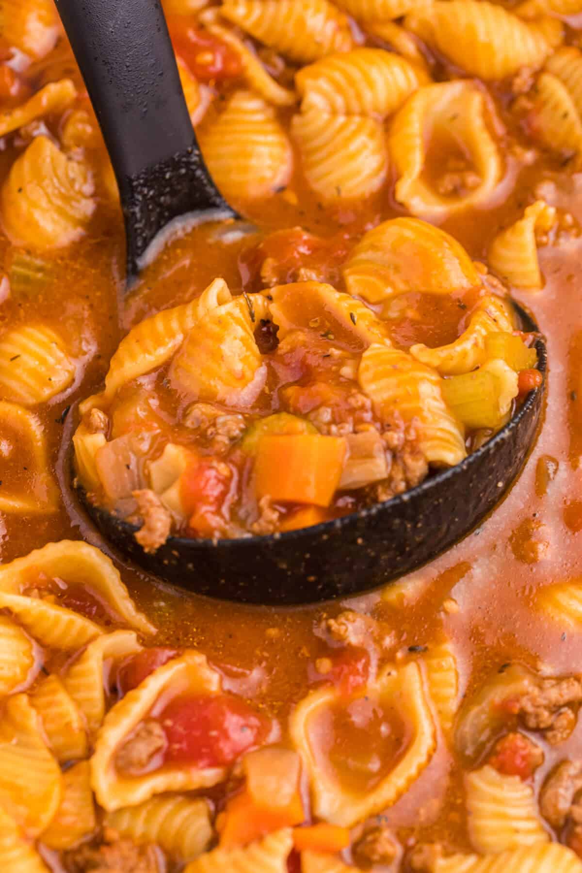 Hamburger soup in a black ladle in a pot of soup.