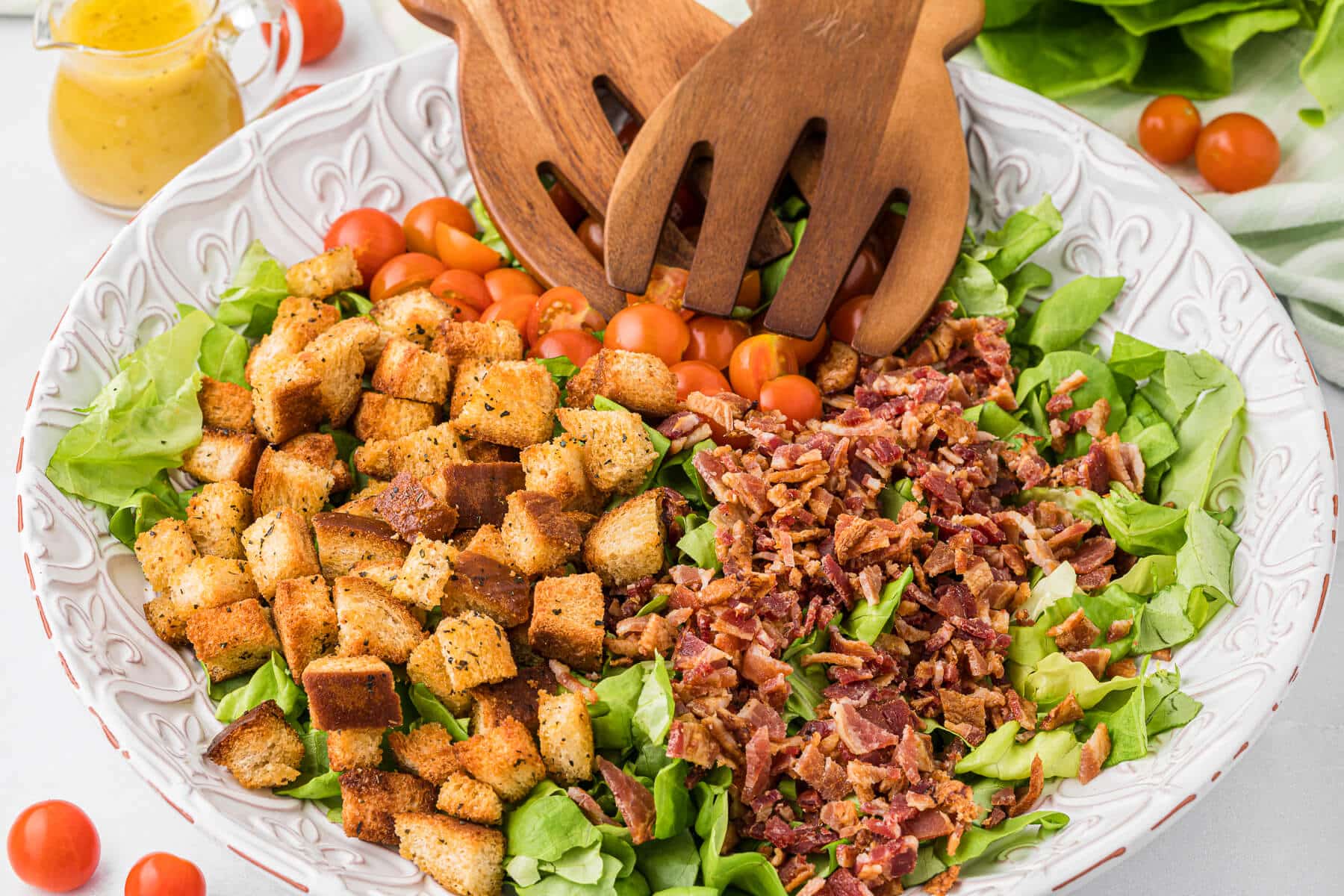 Blt salad in a bowl with wooden salad tongs.