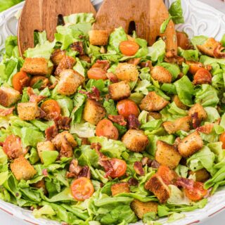 Blt salad in a bowl with wooden salad tongs.