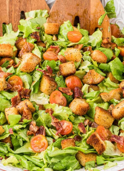 Blt salad in a bowl with wooden salad tongs.