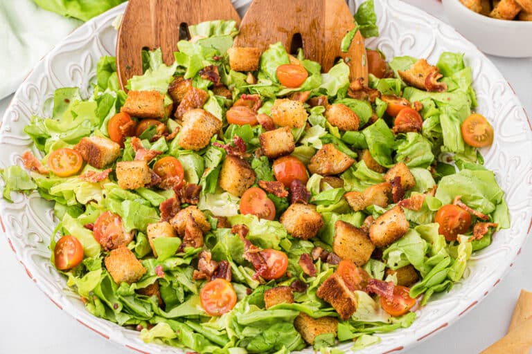 Blt salad in a bowl with wooden salad tongs.