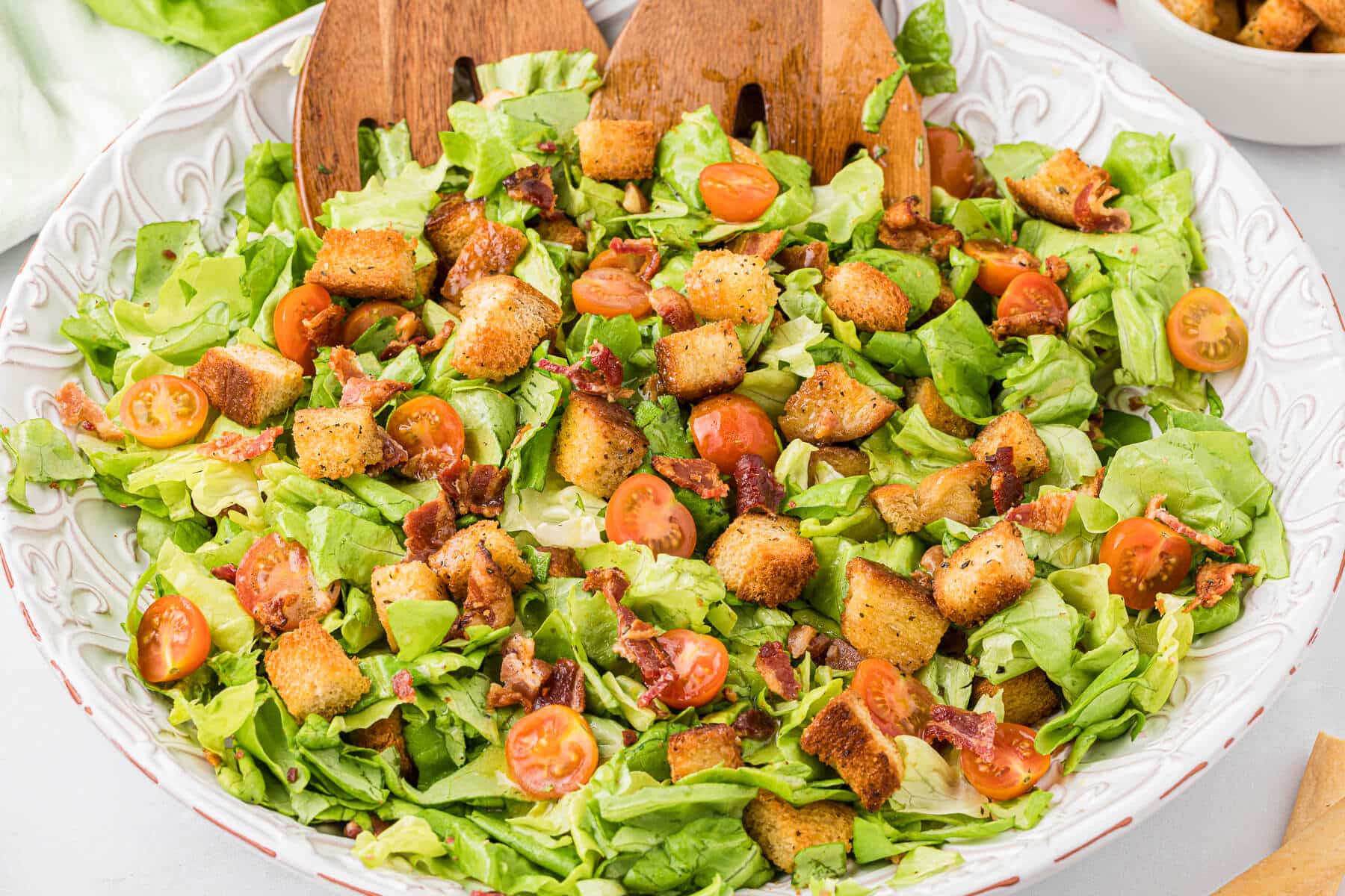 Blt salad in a bowl with wooden salad tongs.