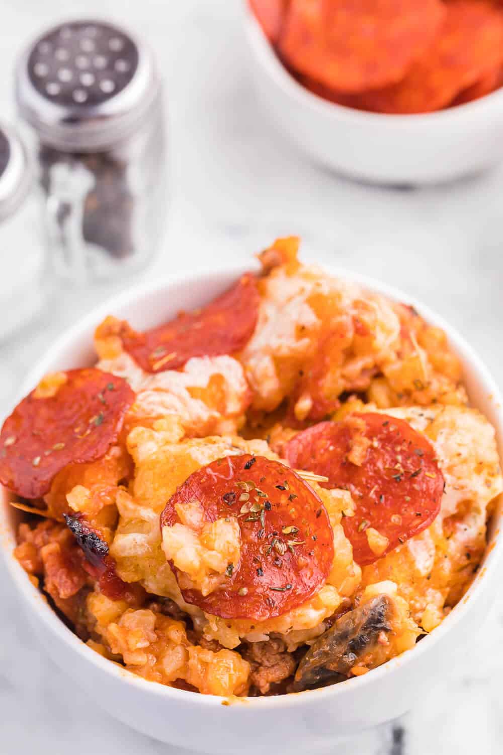 Pizza tater tot casserole served in a white bowl.