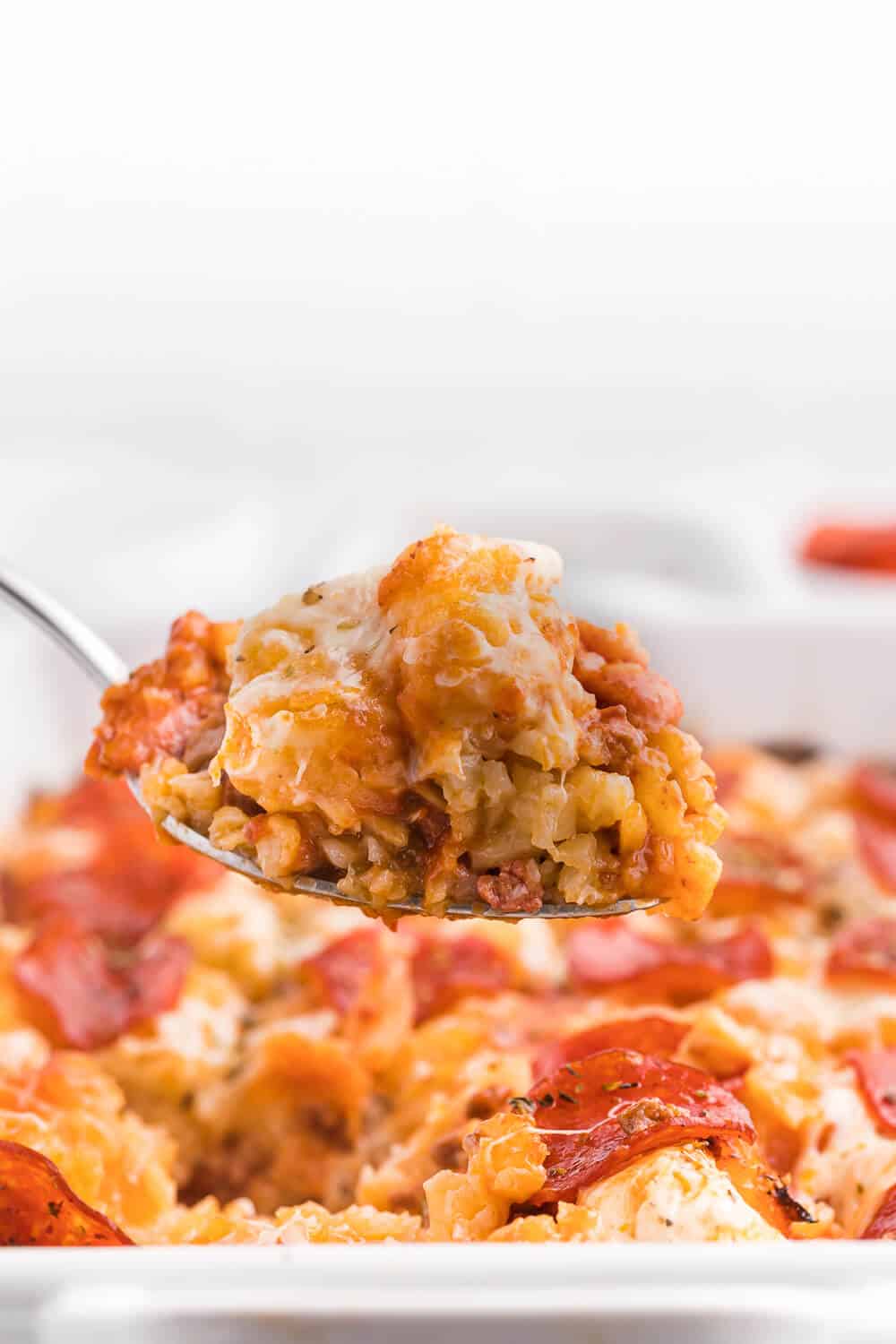 A serving spoon with pizza tater tot casserole on it.