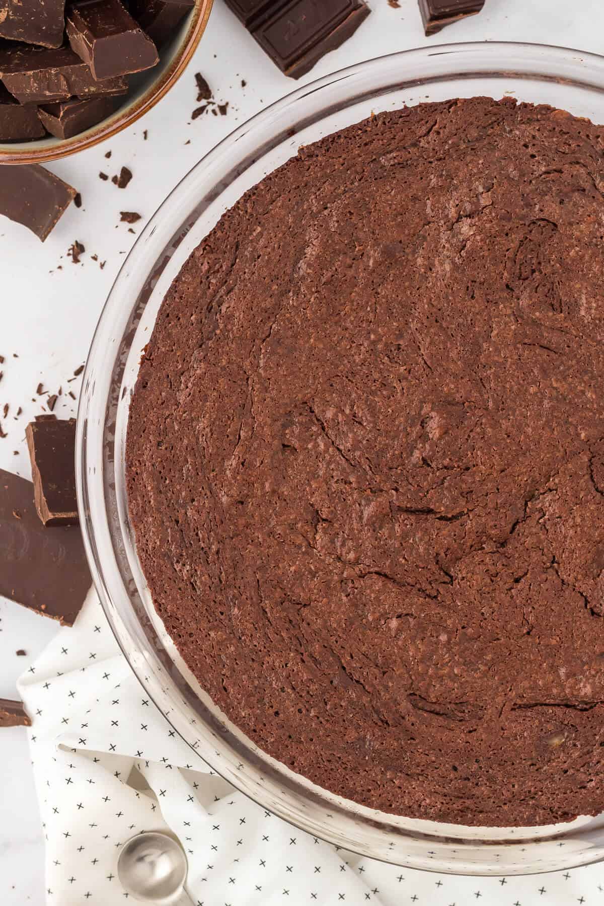 A fudge pie on a white surface surrounded by pieces of chocolate.