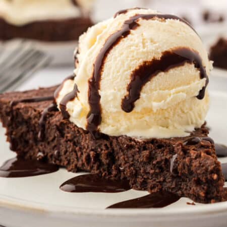 Fudge pie slice topped with vanilla ice cream and chocolate sauce.