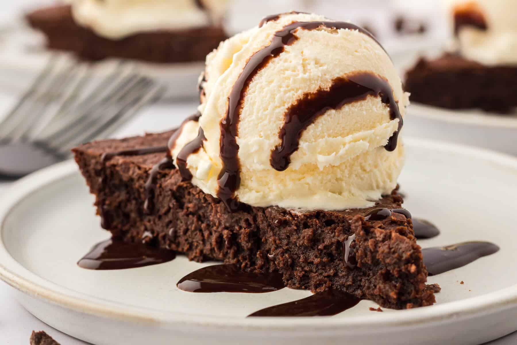 Fudge pie slice topped with vanilla ice cream and chocolate sauce.