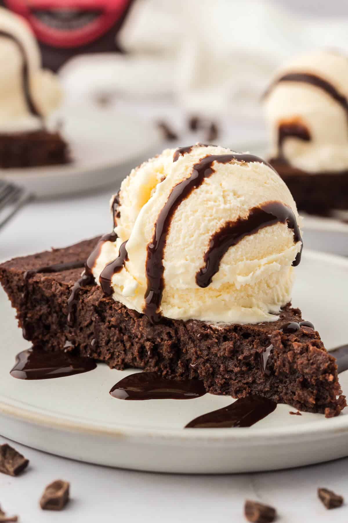 A slice of fudge pie topped with vanilla ice cream and chocolate sauce.