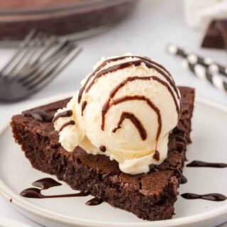 Fudge pie slice on a plate topped with vanilla ice cream and chocolate sauce.