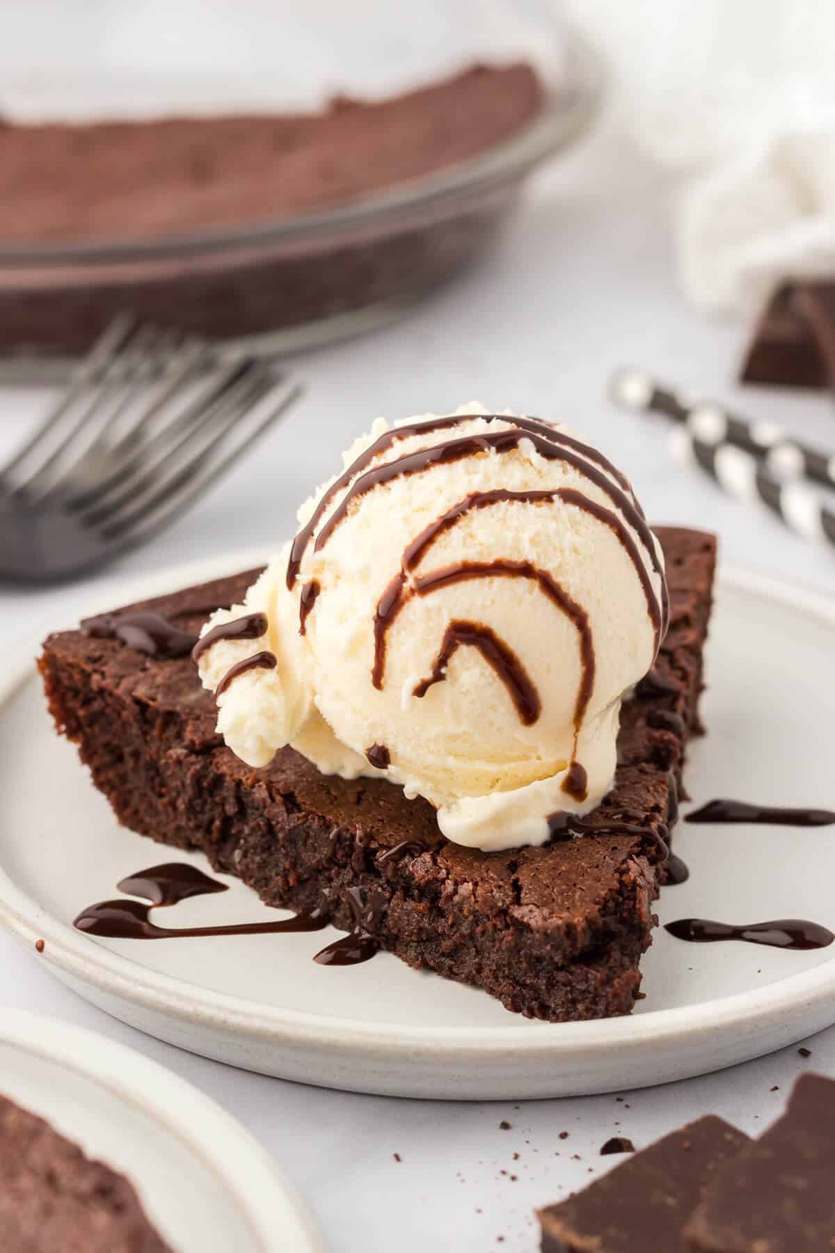 Fudge pie slice on a plate topped with vanilla ice cream and chocolate sauce.