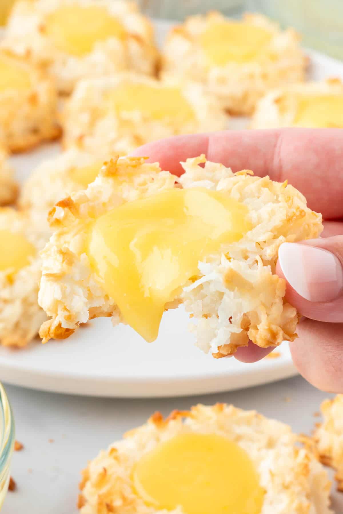 A hand holding a lemon curd coconut macaroons with a bite out of it.