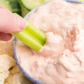 A hand dipping celery in the dip.