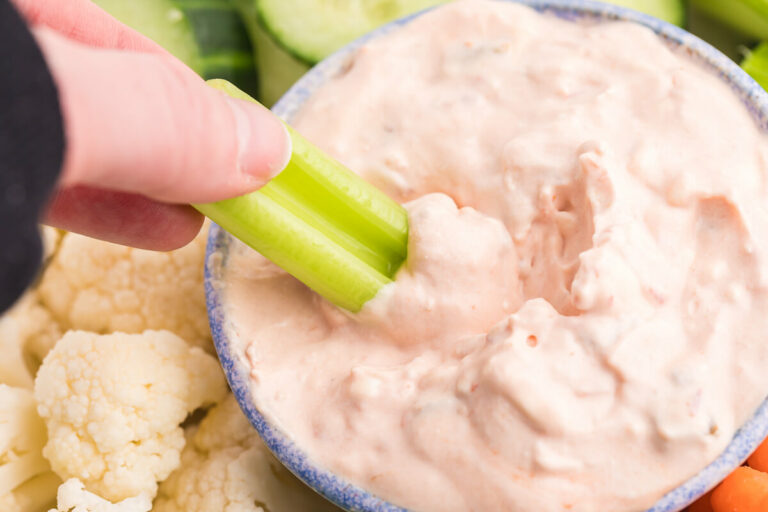 A hand dipping celery in the dip.