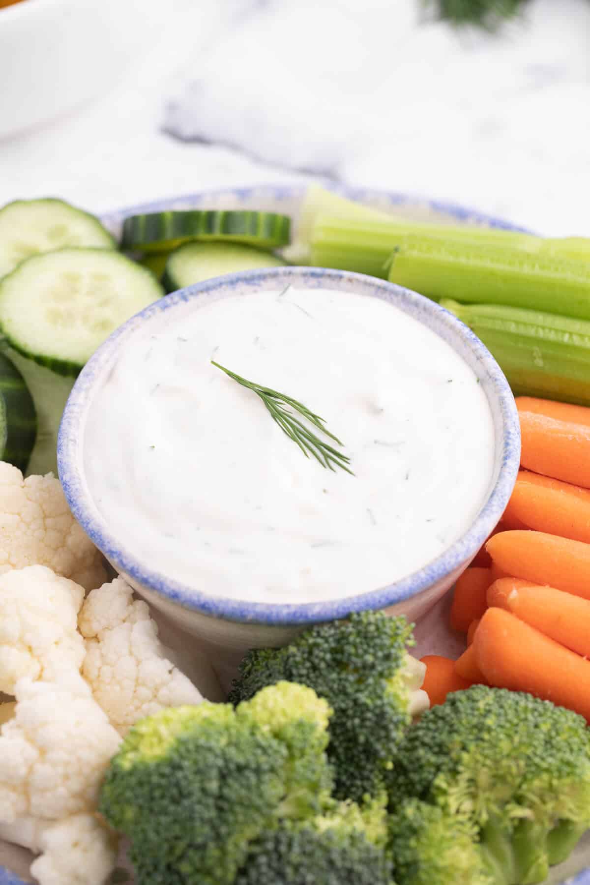 Photo of lemon dill dip in a bowl surrounded by fresh veggies.