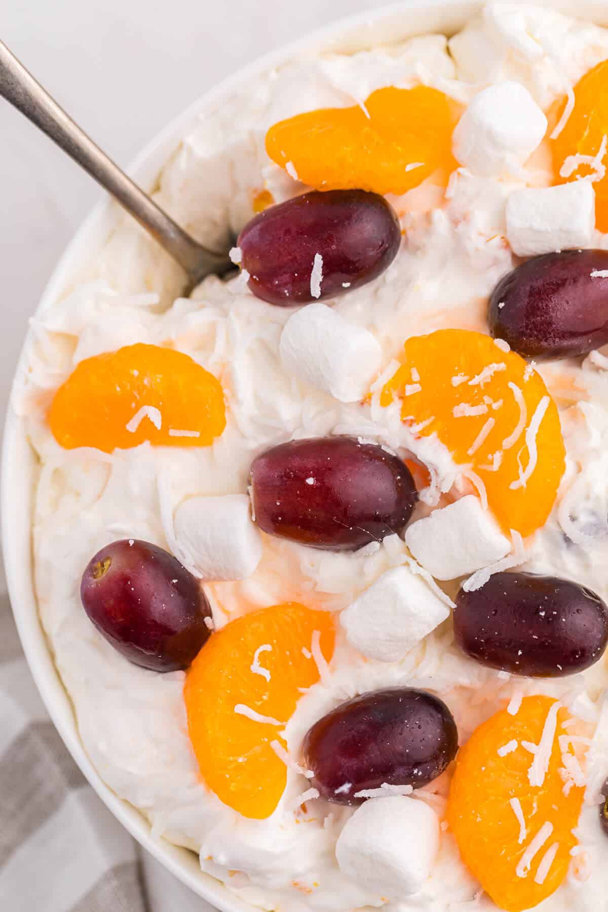 Creamy fruit salad in a bowl with a spoon.