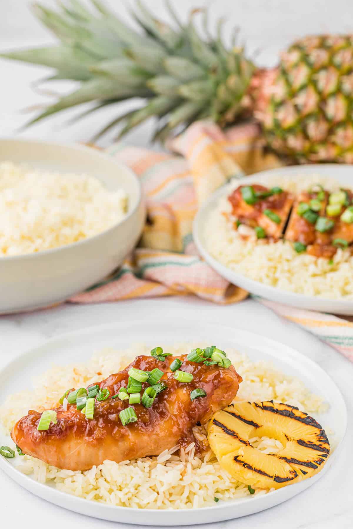 Hawaiian chicken on a plate with rice and a grilled pineapple.