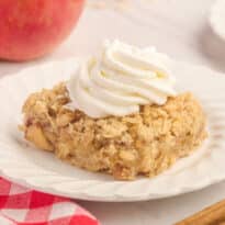 A slice of the recipe topped with whipped cream on a plate.