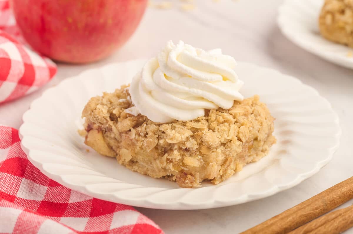 An apple crisp bar topped with whipped cream on a plate.