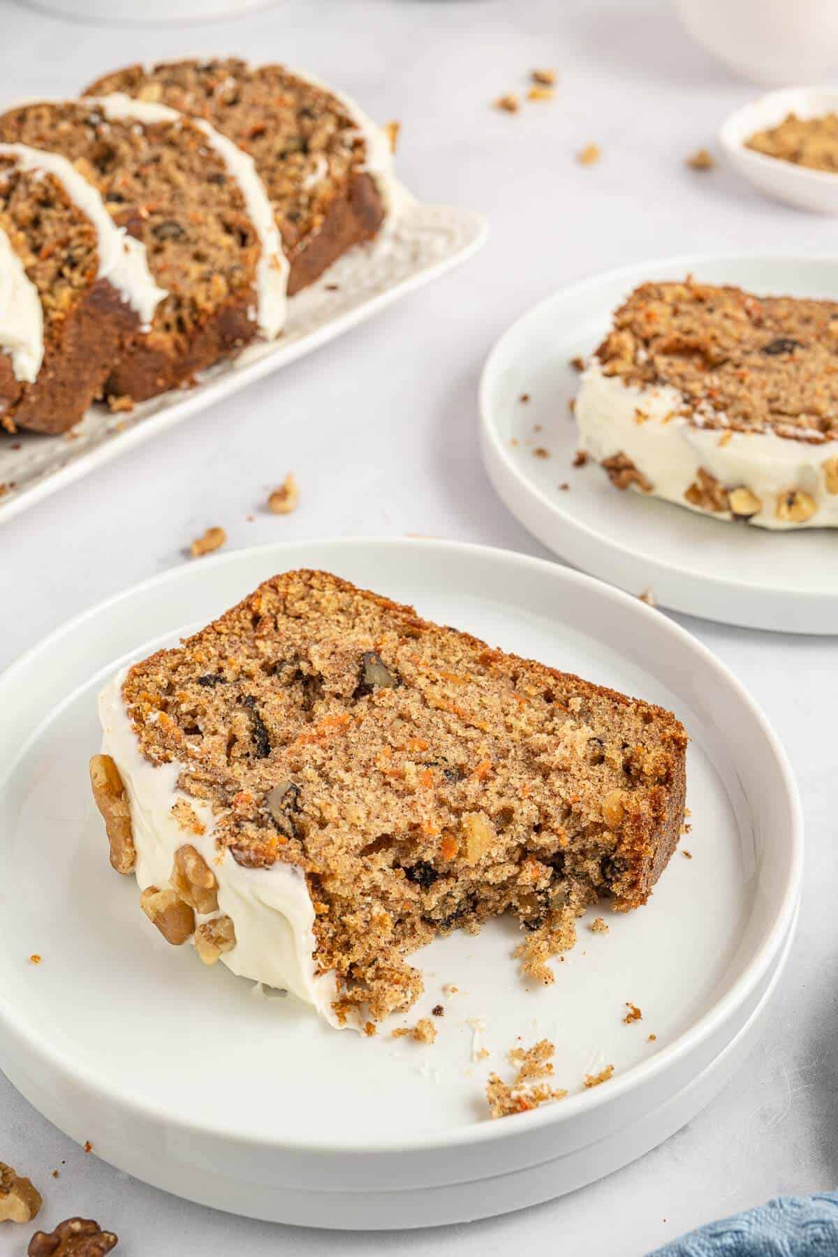 A carrot cake loaf slice on a plate with a bite out of it.