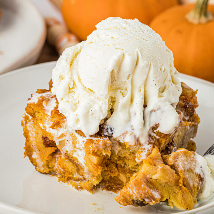 A piece of pumpkin bread pudding topped with vanilla ice cream on a plate with a fork.