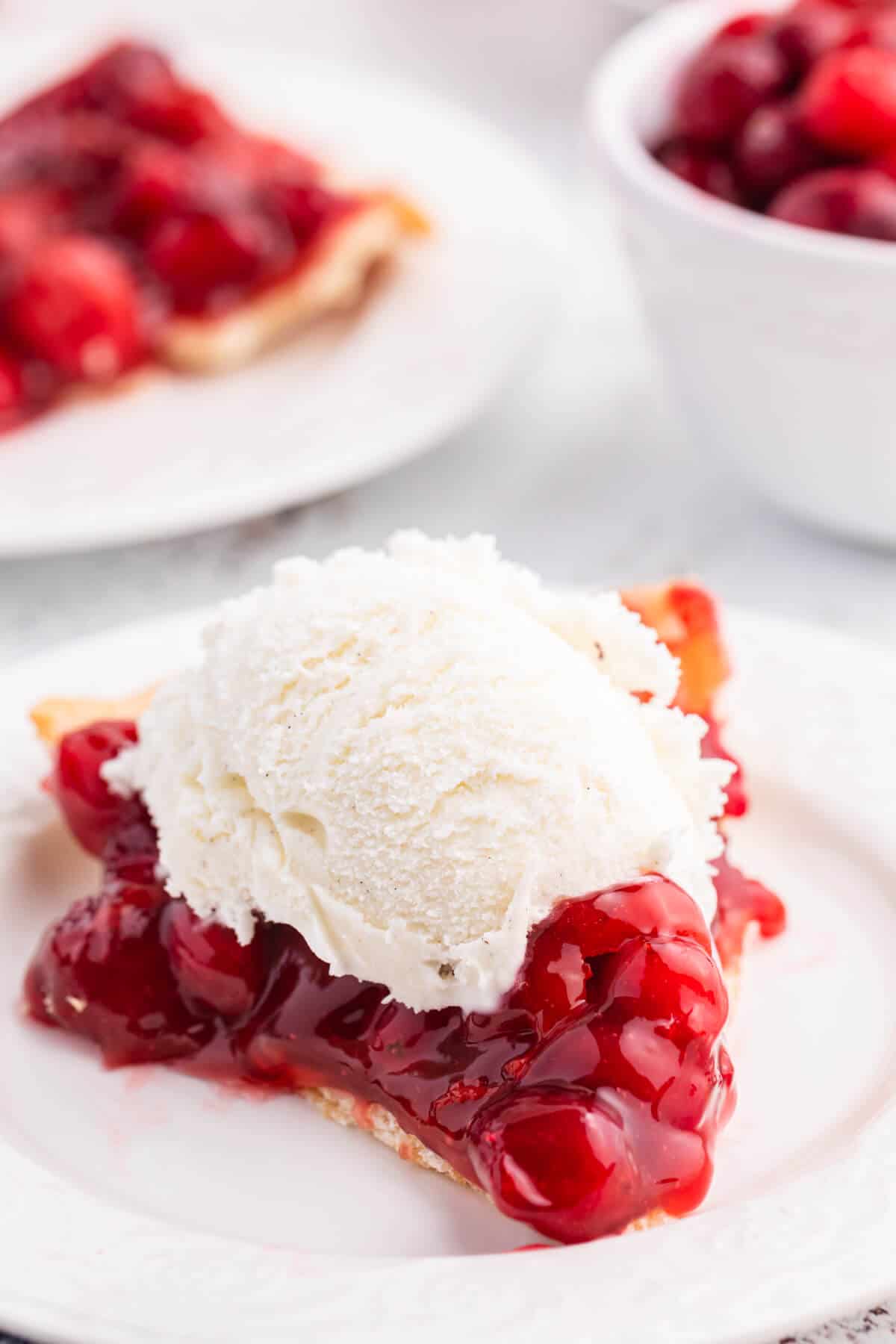 A slice of cherry cranberry pie topped with vanilla ice cream.