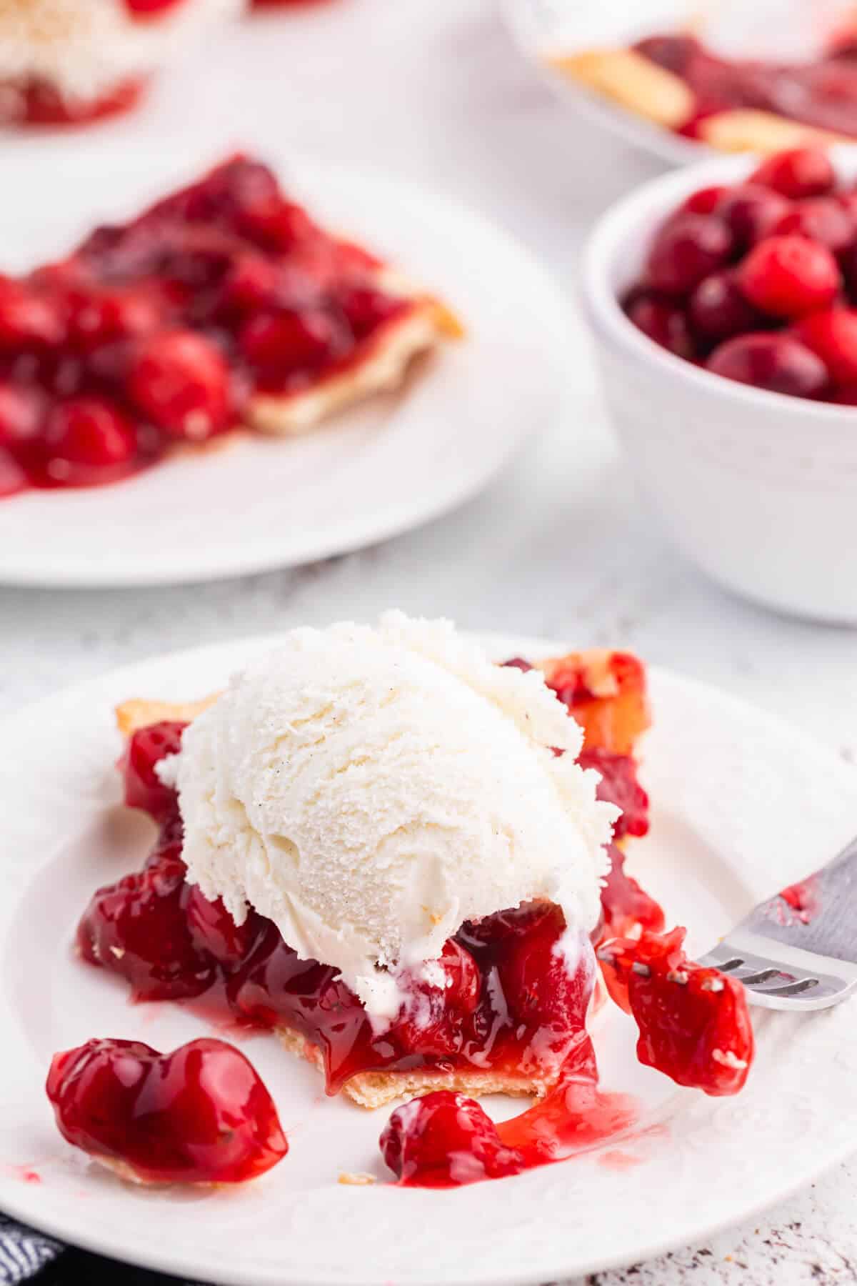 A slice of cherry cranberry pie on a plate topped with vanilla ice cream.