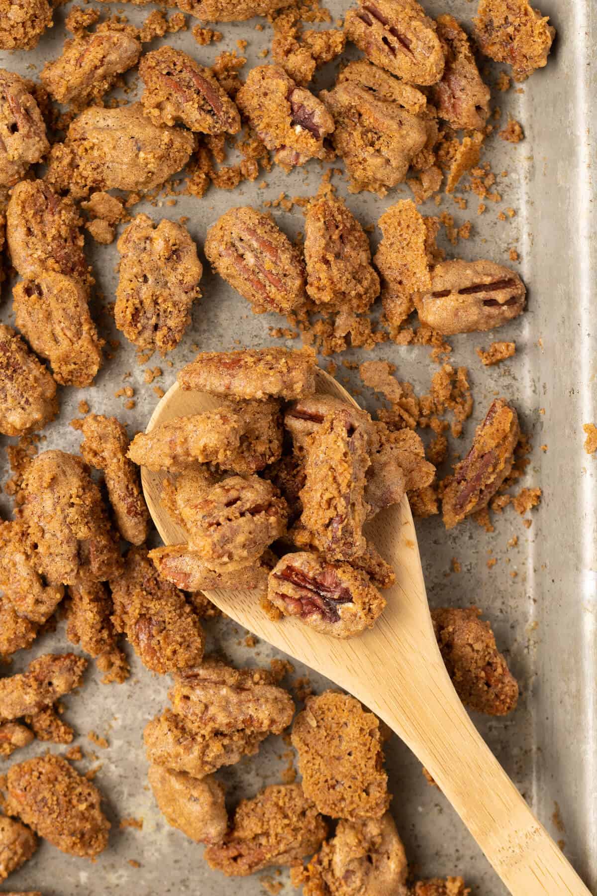 Sweet spiced pecans on a baking sheet with a wooden spoon.