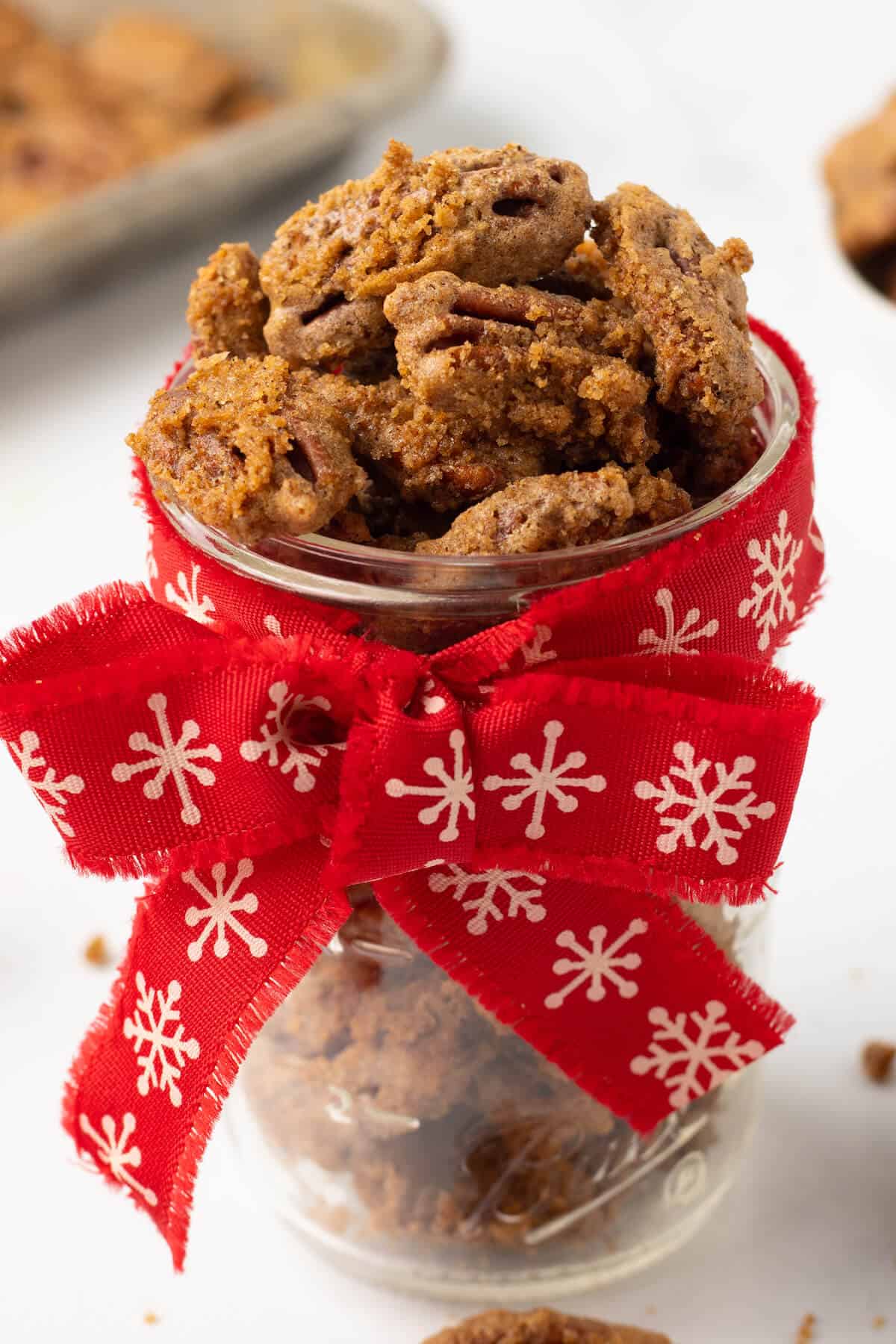 Sweet spiced pecans in a jar with a red festive bow.