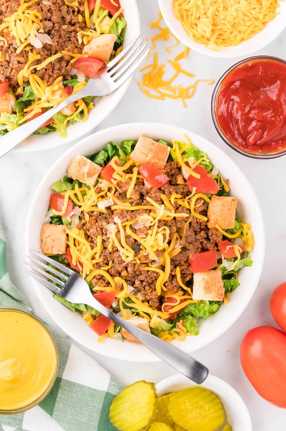 A bowl of cheeseburger salad surrounded by ingredients.