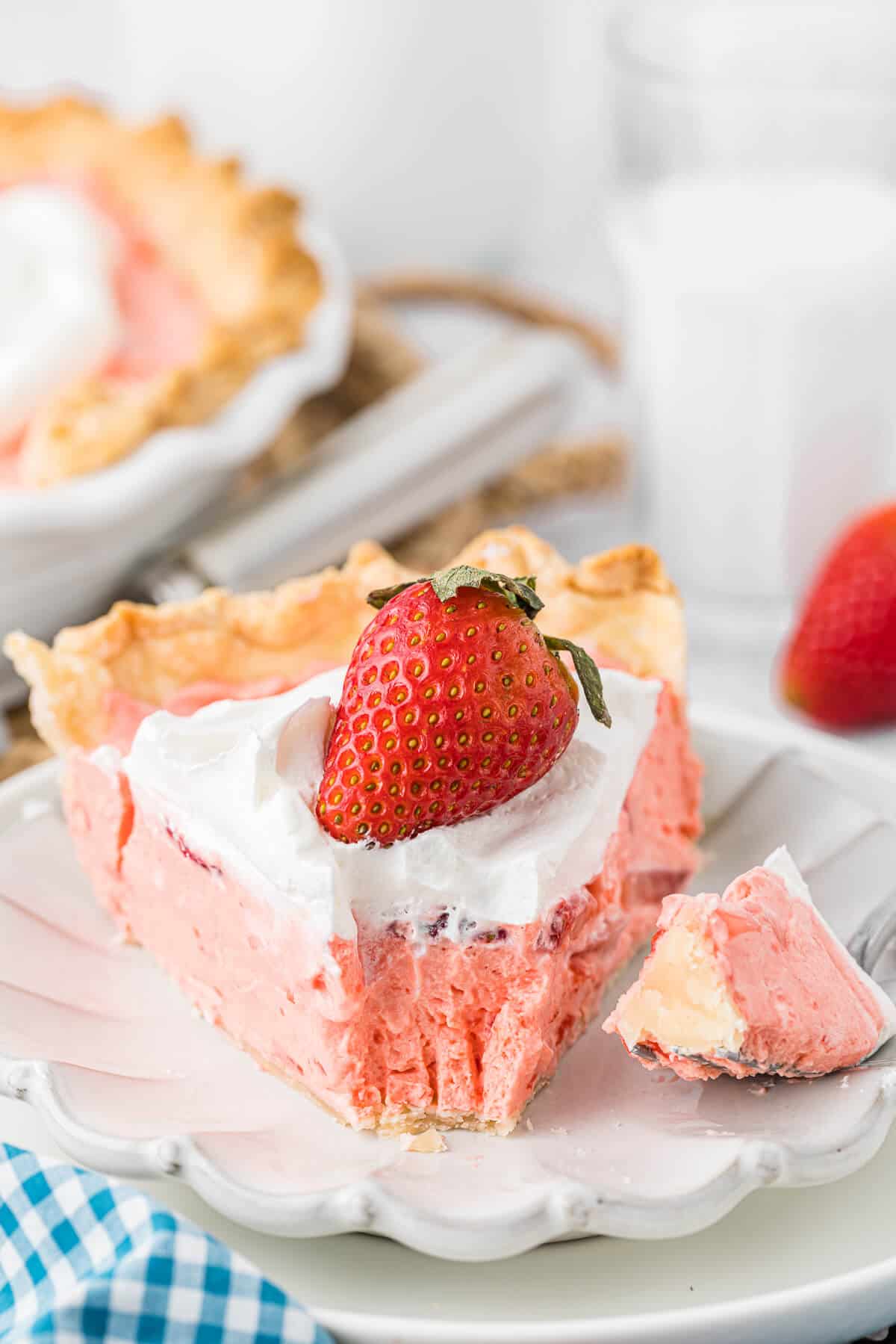 A slice of strawberry cream pie on a plate with a fork and bite off the end.