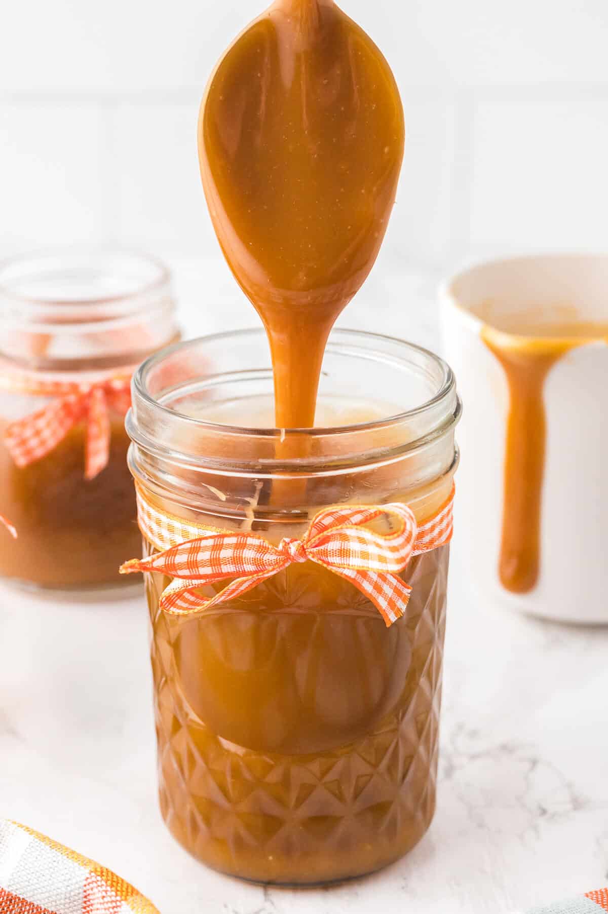 A spoon drizzling butterscotch sauce in a jar.