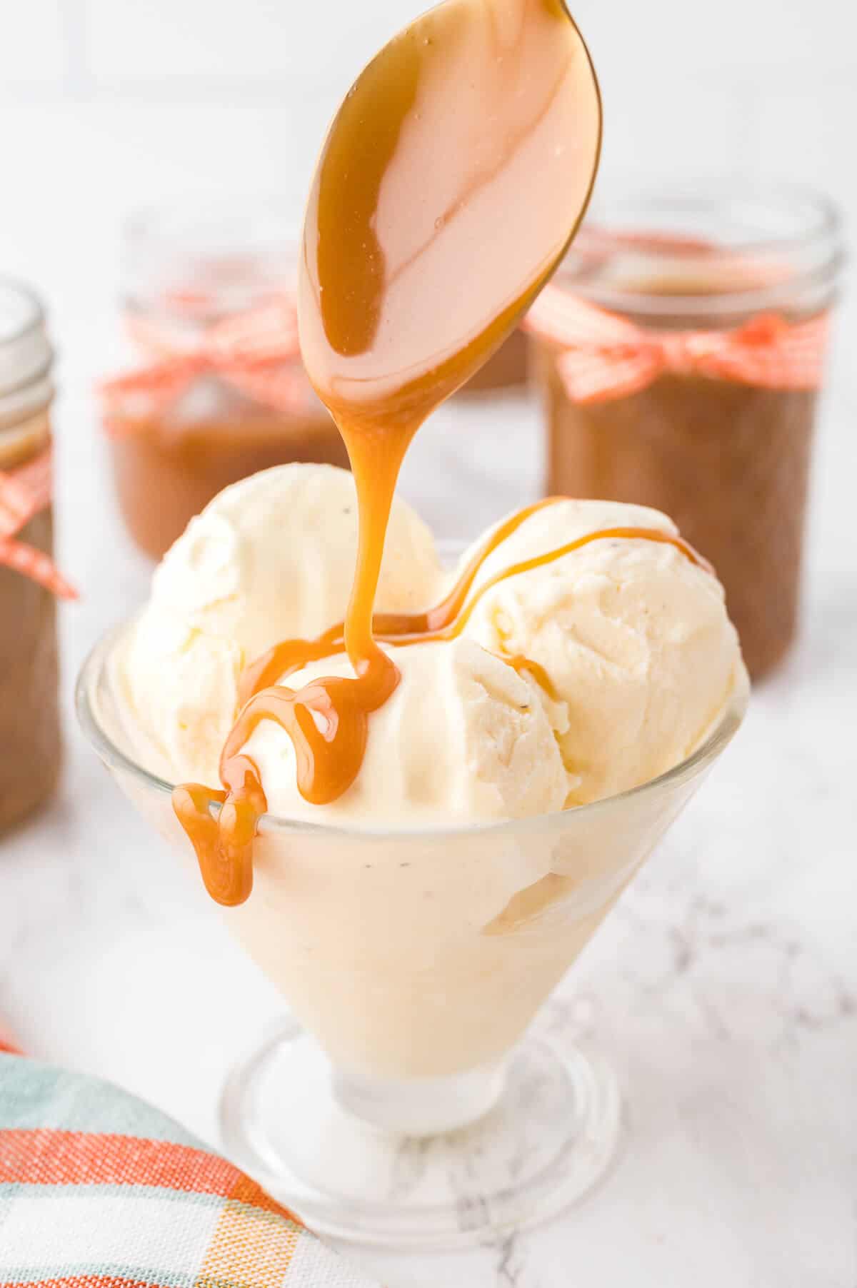 A spoon drizzling butterscotch sauce over vanilla ice cream.