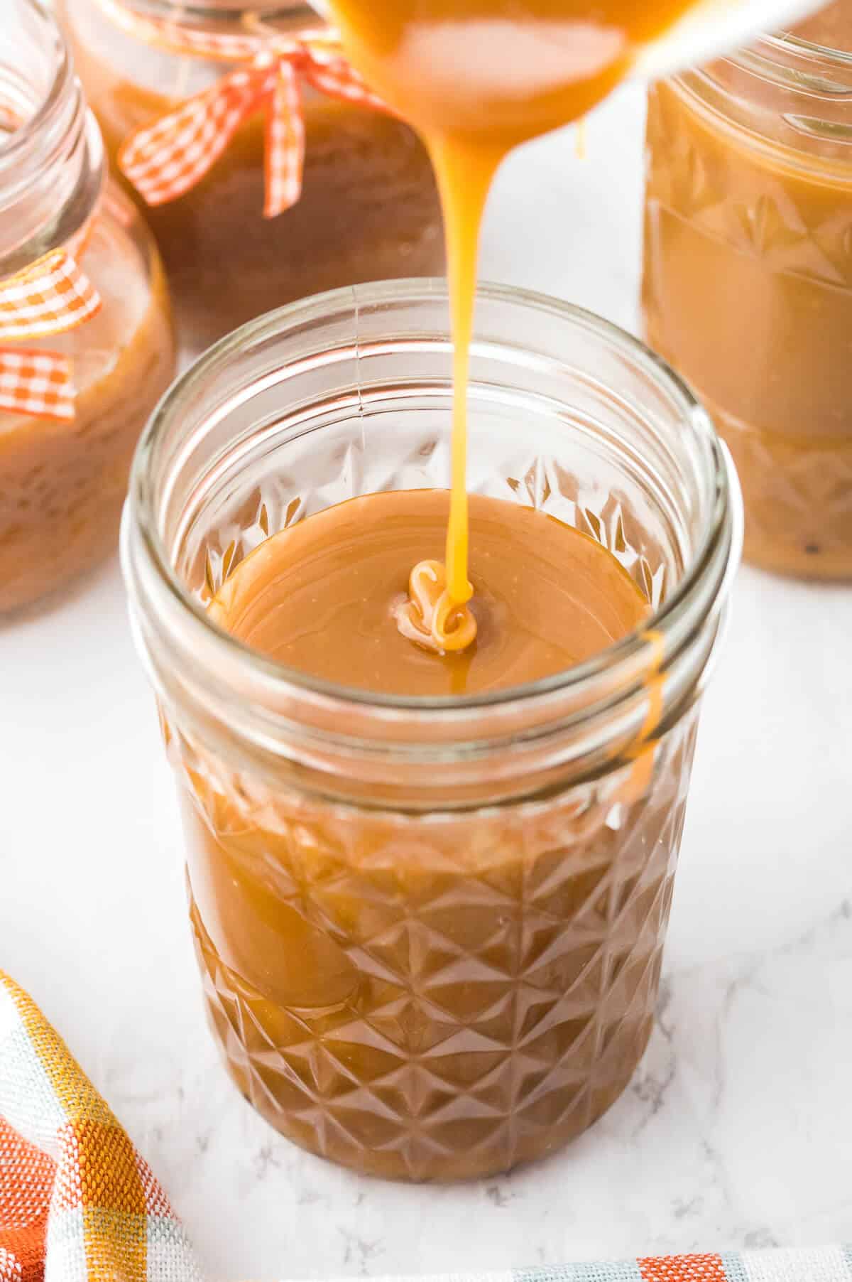 Butterscotch sauce in a jar with a spoon drizzling sauce inside.