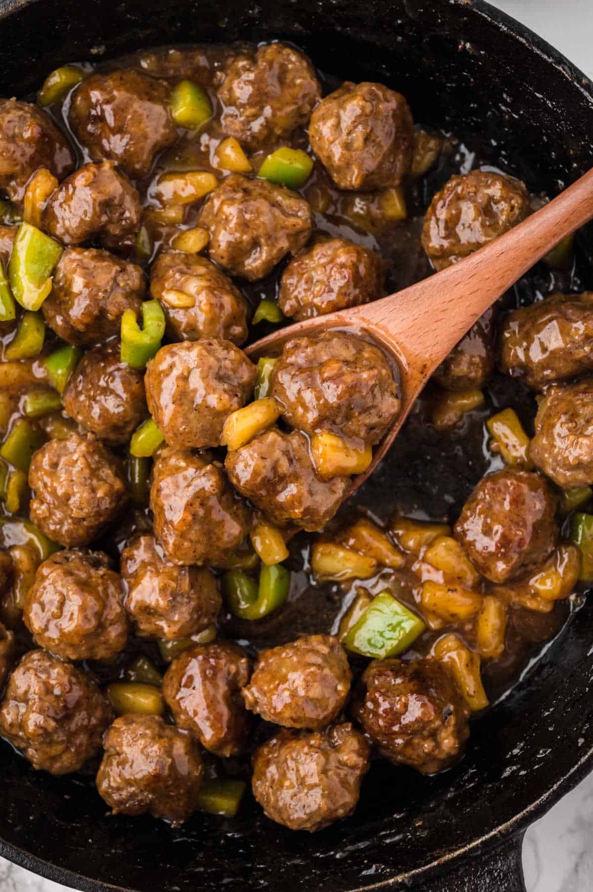 Waikiki meatballs in a skillet with a wooden spoon.