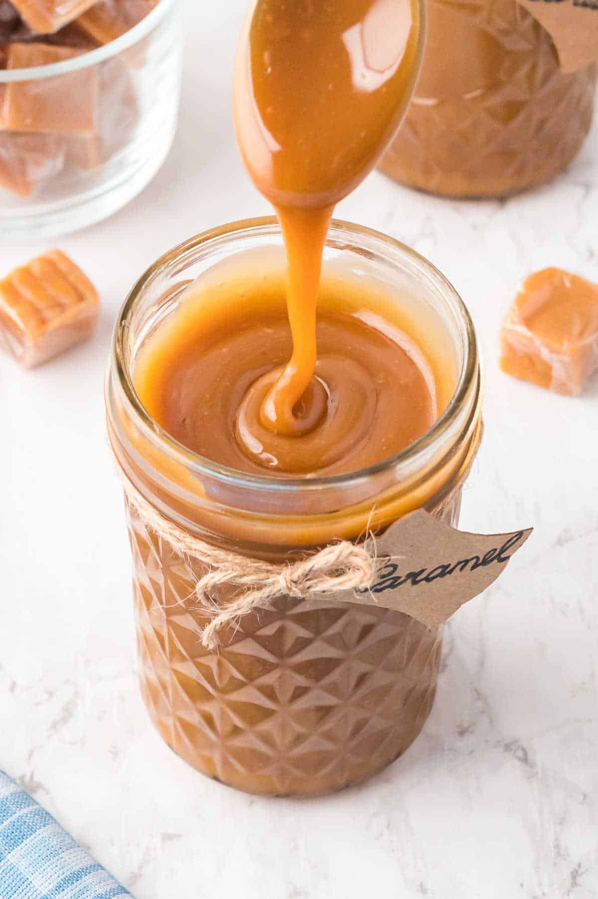 Caramel sauce being drizzled into a glass jar from a spoon.