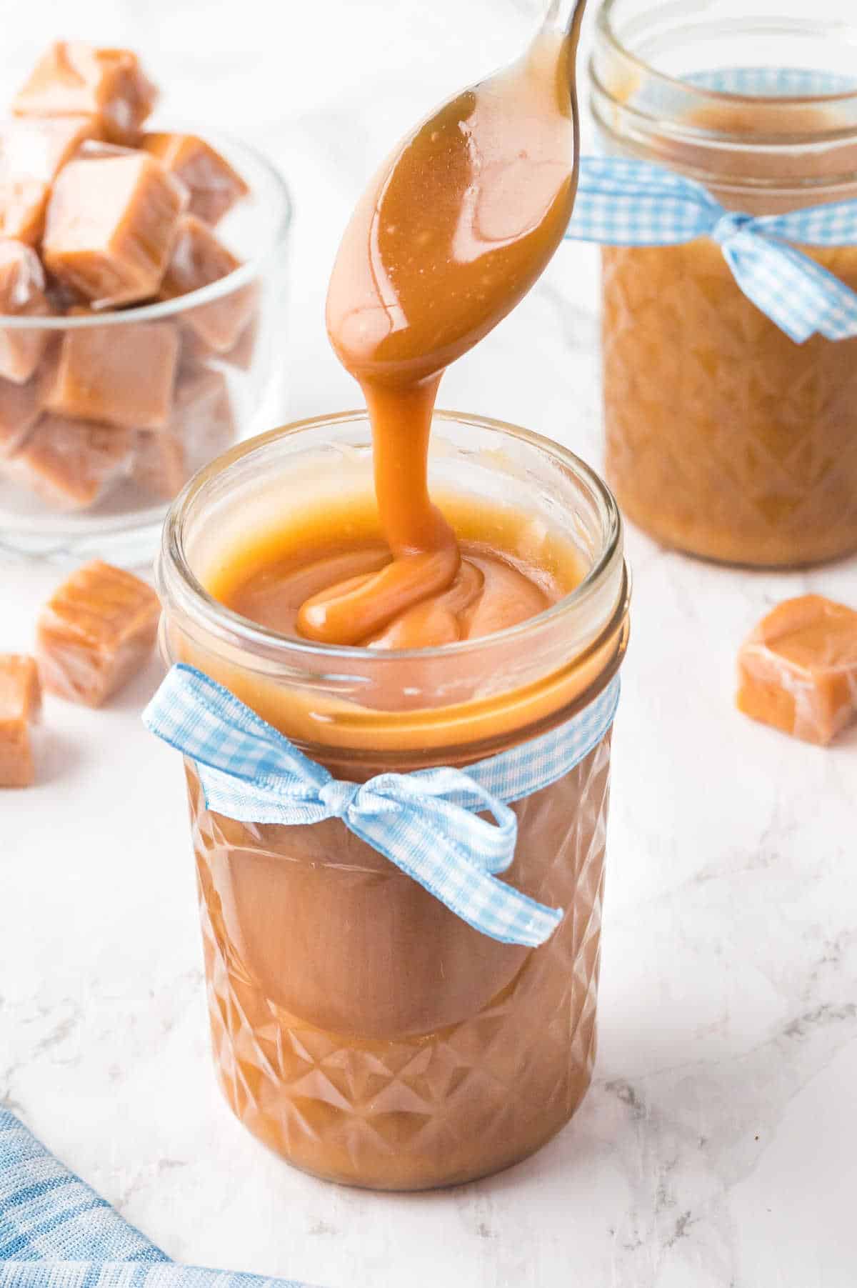 Caramel sauce in a glass jar and coming off a spoon over the jar.