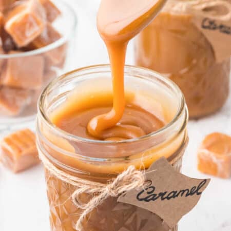 A spoon drizzling caramel sauce in a jar.